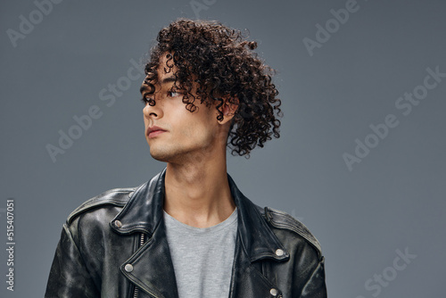 Pensive handsome stylish tanned curly man leather jacket looks aside posing isolated on over gray studio background. Cool fashion offer. Huge Seasonal Sale New Collection concept. Copy space for ad