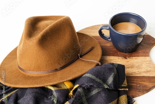 Closeup shot of a cup of coffee, a hat, and a scarf on a wooden board photo