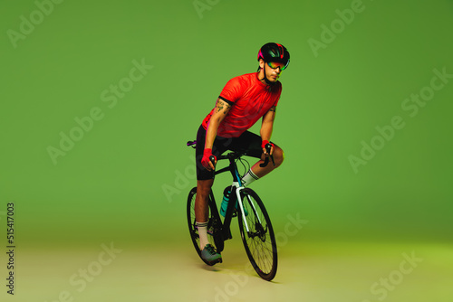 Male cyclist riding bicycle in sports uniform and protective helmet isolated on green studio background. Concept of active life, rest, travel, energy, sport