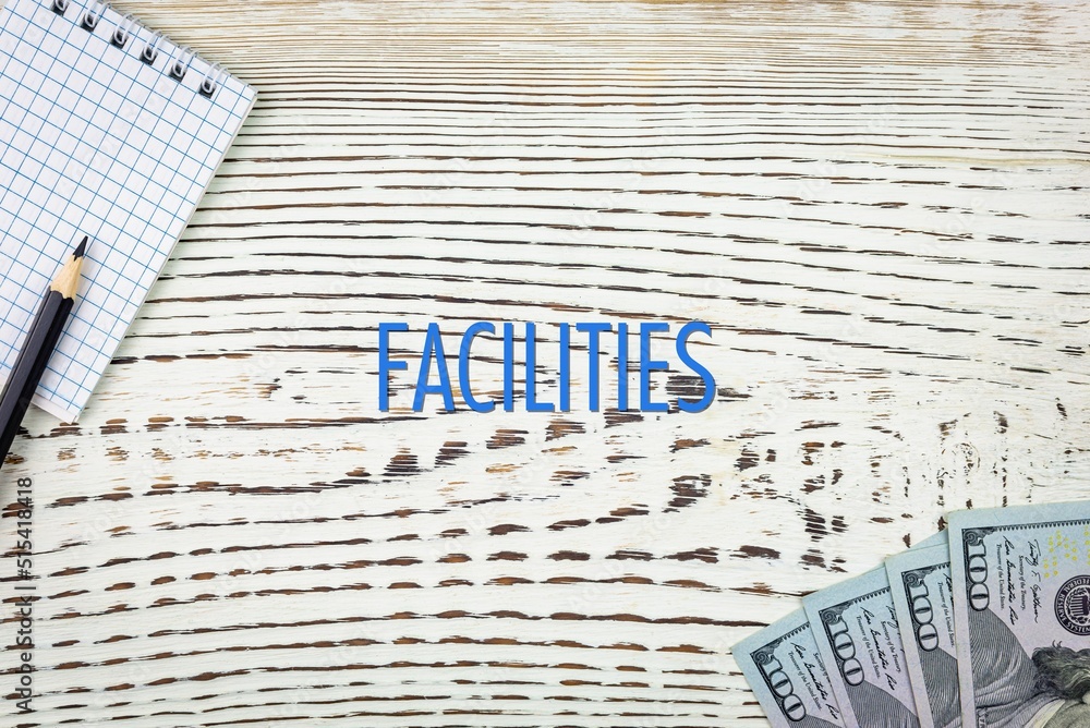 Naklejka premium FACILITIES - word (text) and dollars on a white wooden table, notebook, notepad. Business concept: buying, selling, commerce (copy space).