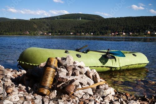 A tourist thermos lies on a rocky shore, to which an inflatable boat is moored. 
