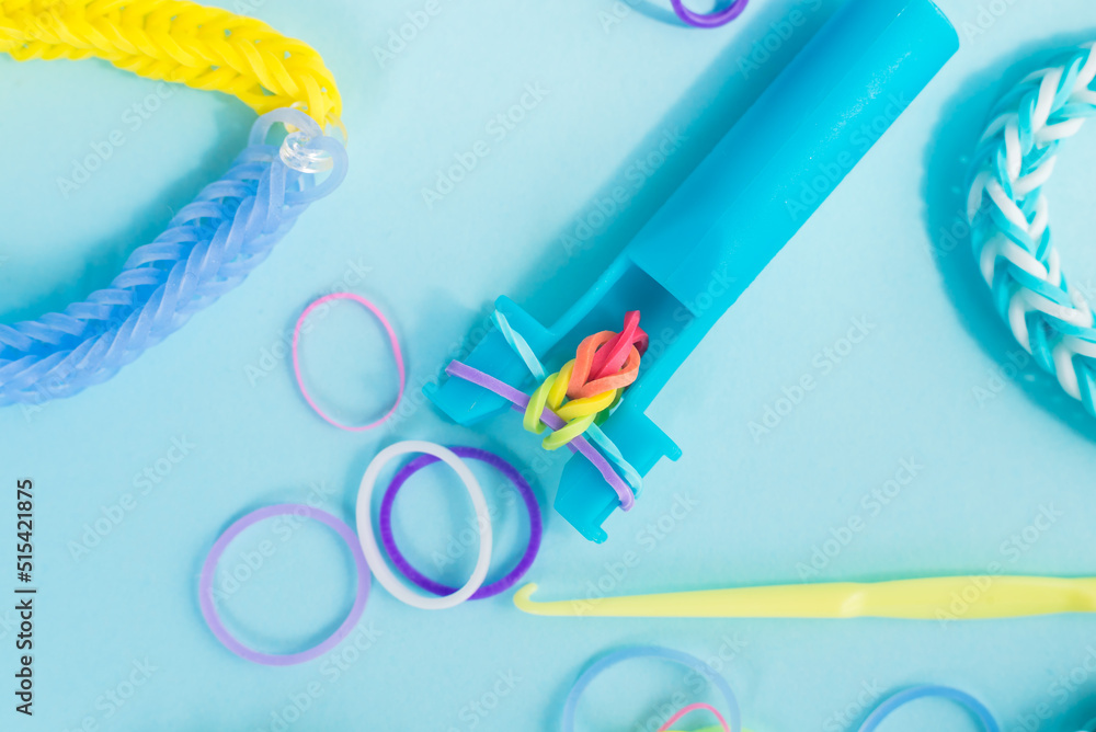 Fototapeta premium Closeup of making decorative bracelet with elastic bands on blue backround. Loom bracelets