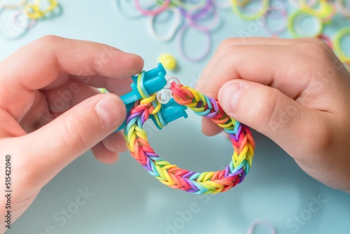 A girl makes a rainbow bracelet from rubber bands crochet. Closeup of making decorative bracelet with elastic bands. Loom bracelets