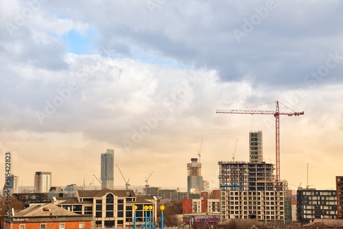 City view with modern buildings and construction work with large cranes. Manchester skyline at sunset. 