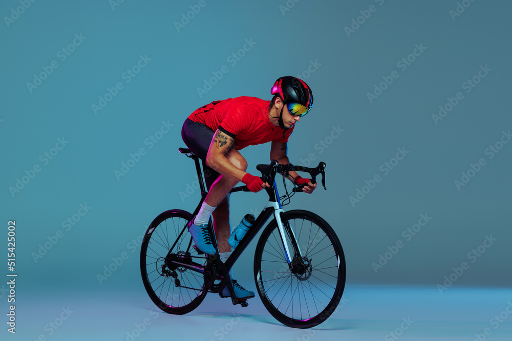 Obraz premium Studio shot of professional cyclist in red sports uniform, goggles and a helmet on a blue background. Concept of active life, rest, travel, energy, sport
