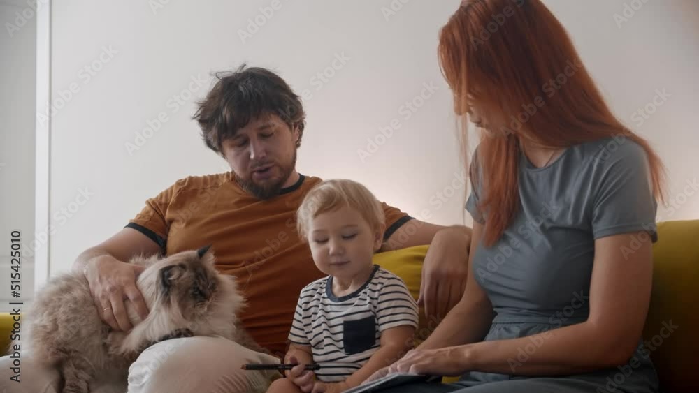 Family sitting on yellow couch with their fluffy cat pet Family sitting on yellow couch with their fluffy cat pet