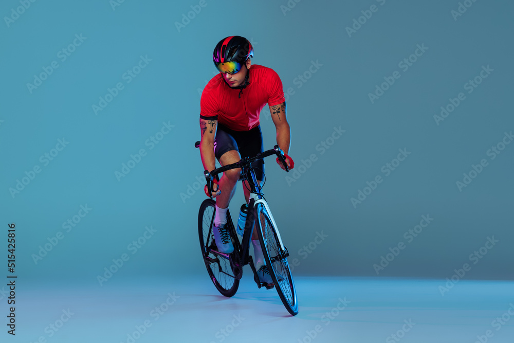 Obraz premium Studio shot of professional cyclist in red sports uniform, goggles and a helmet on a blue background. Concept of active life, rest, travel, energy, sport