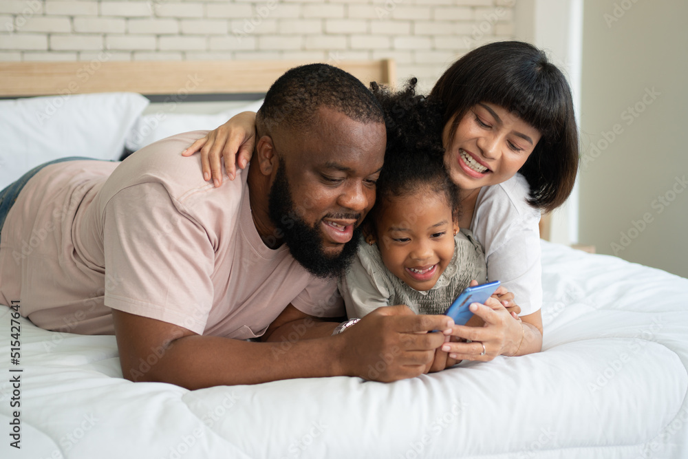 The family has fun and plays education games online with a smartphone at home in the bedroom. Concept of online education and caring from parents.