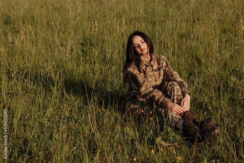 Female soldier sitting on grass in the field dressed in military uniform. Armed Forces of Ukraine. Woman serving in ukrainian army.