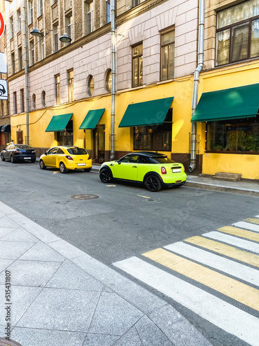 Colorful cars parked near a yellow wall on a city street. © Natalia