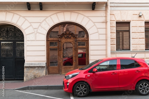 Art Nouveau wooden front door and red car in front of it. Cityscape. © Natalia