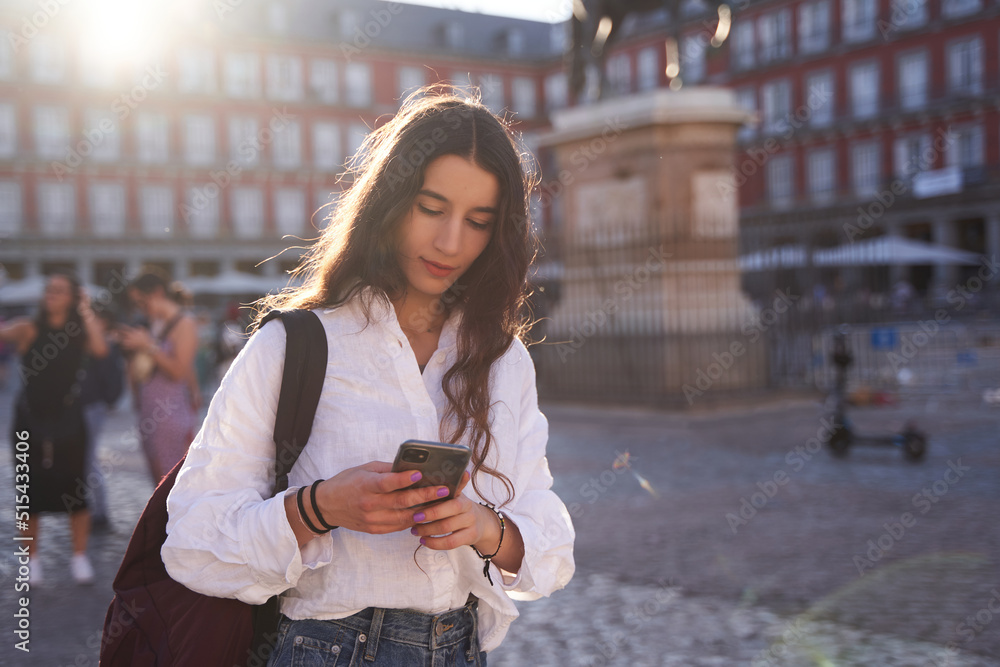 Happy young woman looking at smartphone near the Equestrian Monument to King Philip III of Spain in Madrid's Plaza Mayor. Happy young woman looking at smartphone near the Equestrian Monument to King Philip III of Spain in Madrid's Plaza Mayor.