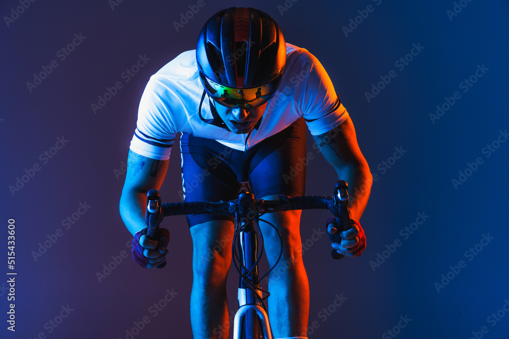 Closeup portrait of professional male cyclist in sports uniform, goggles and helmet on blue background in neon. Concept of sport fashion, race, competition Closeup portrait of professional male cyclist in sports uniform, goggles and helmet on blue background in neon. Concept of sport fashion, race, competition