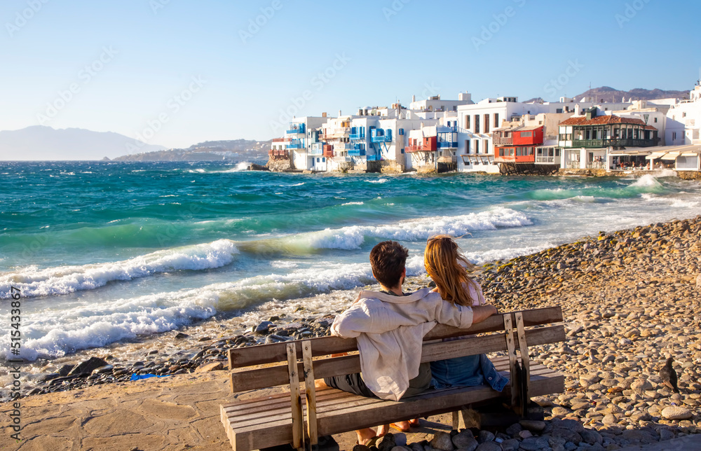 Romantic young couple sitting against the waves, Mykonos island, Greece, famous Little Venice area of Mykonos town