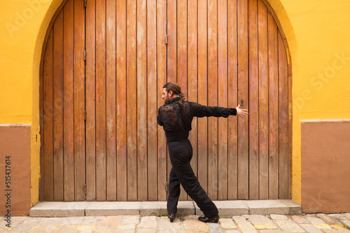 man dancing flamenco with black shirt and red roses, on a background of a wooden door, doing different postures while dancing. Flamenco dance concept cultural heritage of humanity. Feel de passion.