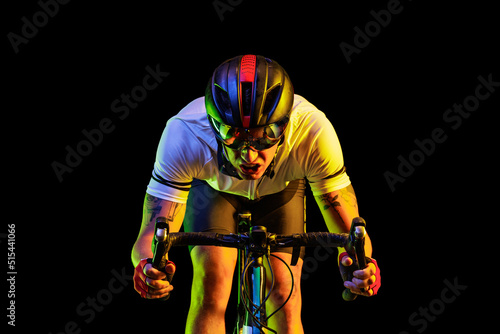 Portrait of professional male cyclist in sports uniform, goggles and helmet on dark background in yellow neon light. Concept of sport fashion, race, competition