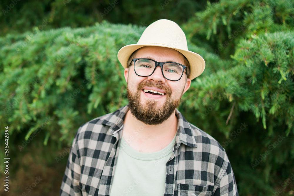 Laughing attractive man wearing hat over green tree background - emotion and vacation travel holidays concept