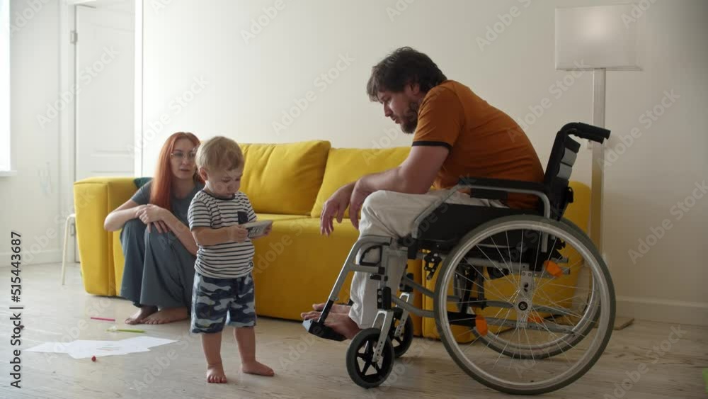 Man in a wheelchair helps his little baby son to fix a TV remote Man in a wheelchair helps his little baby son to fix a TV remote