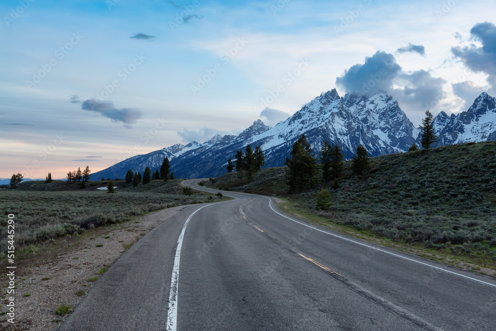 Naklejka premium Scenic Road surrounded by Mountains and Trees in American Landscape. Spring Season. Grand Teton National Park. Wyoming, United States. Nature Background.