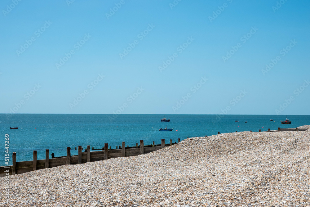 deserted beach with bank of pebbles and sea and sky in the background with fishing boats