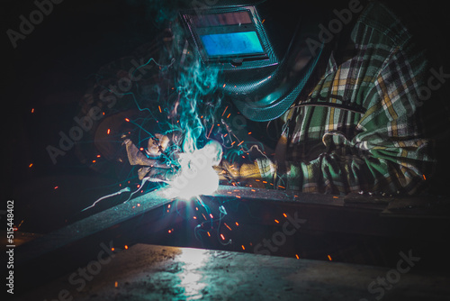 A male welder works with a welding machine in the garage, orange sparks fly to the sides.