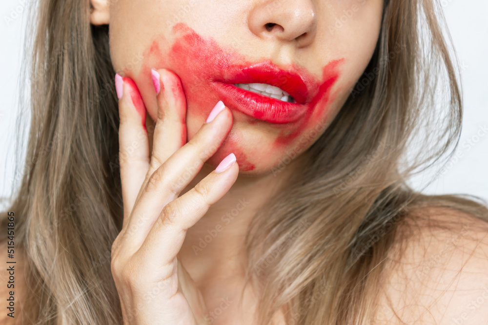 Fototapeta premium Cropped shot of a young caucasian blonde woman with perfect lips smearing glossy red color lipstick on the face with her hand isolated on a white background. Beauty and fashion concept