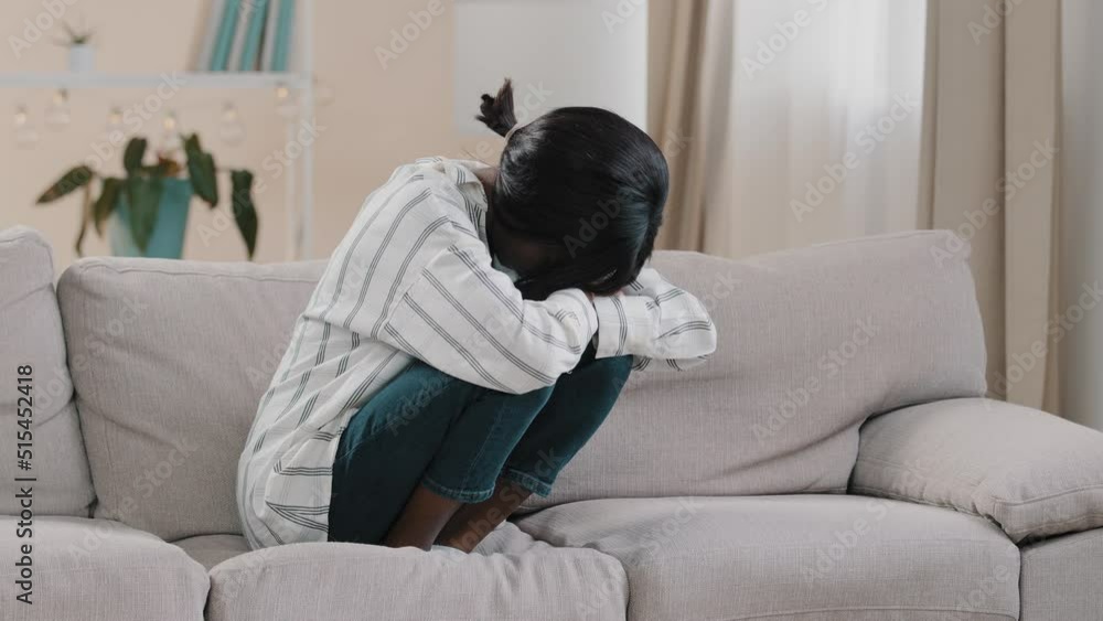 Young tense depressed sad woman sitting on sofa hugging knees thinking about personal problems frustrated stressed girl suffering from troubles worrying about wrong decision needs psychological help Young tense depressed sad woman sitting on sofa hugging knees thinking about personal problems frustrated stressed girl suffering from troubles worrying about wrong decision needs psychological help