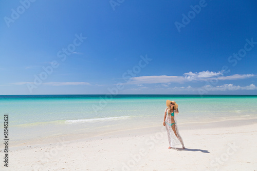 Beautiful sexy young woman in blue bikini and straw hat on the sandy beach. Summer vacations, travel and tourism concept after end of coronavirus covid-19 lockdown