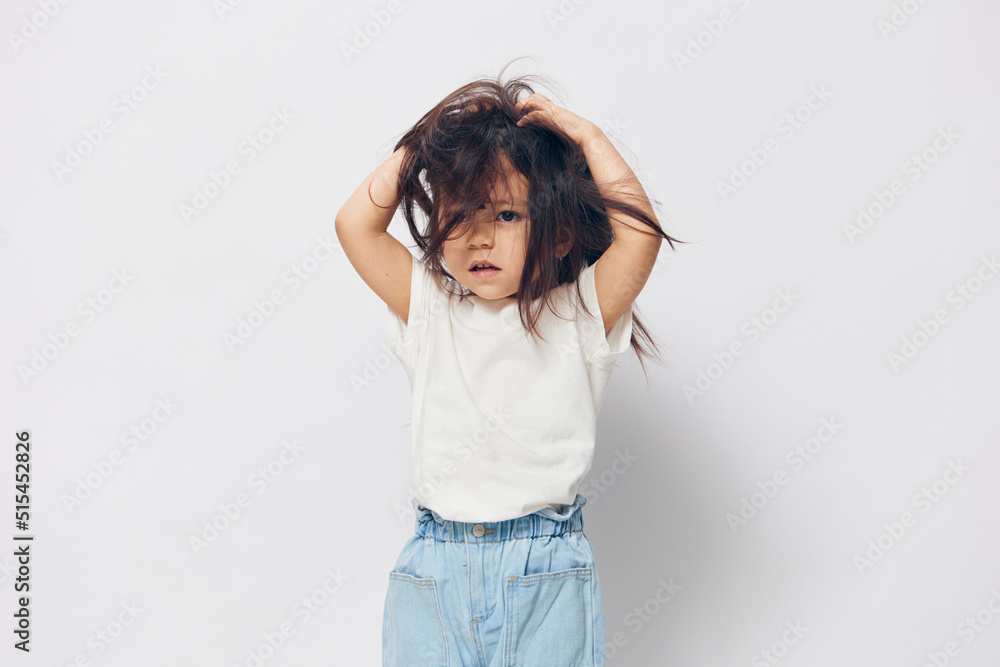 funny, cute, little girl stands in a white T-shirt on a light background and raises her hair on her head up funny, cute, little girl stands in a white T-shirt on a light background and raises her hair on her head up