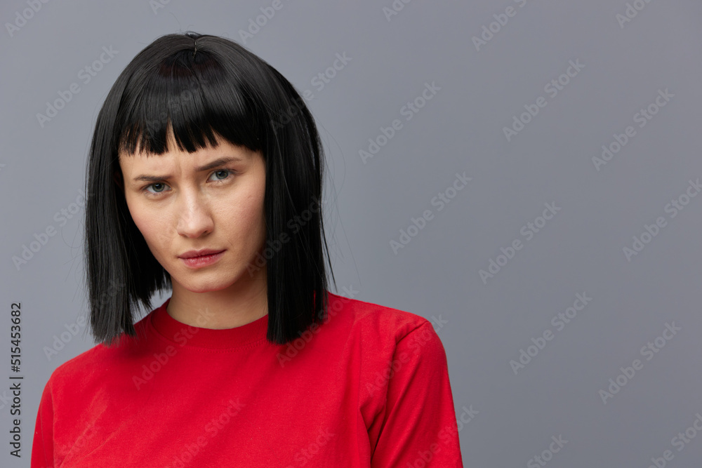 horizontal photo of a sad, upset woman in a red T-shirt on a gray background looking at the camera with a strained look horizontal photo of a sad, upset woman in a red T-shirt on a gray background looking at the camera with a strained look