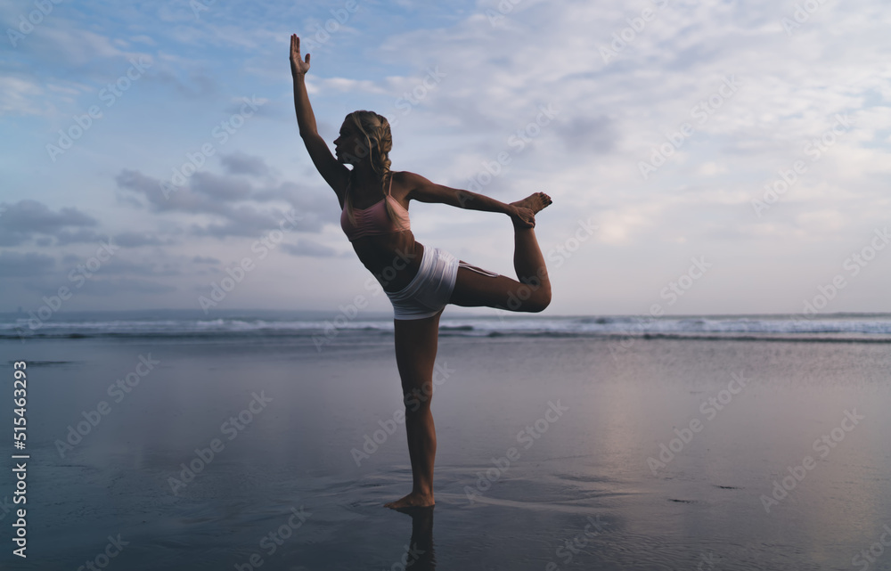 Obraz premium Full length view, Caucasian female with sporty body doing stretching exercises on seashore while training outdoors. Young woman working out and enjoying healthy lifestyle at nature. Warm up on beach