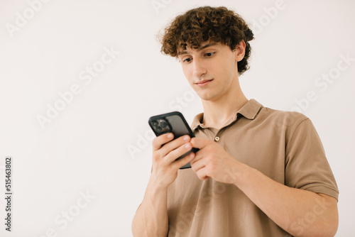 Attractive young male student using the phone on a white background with free space