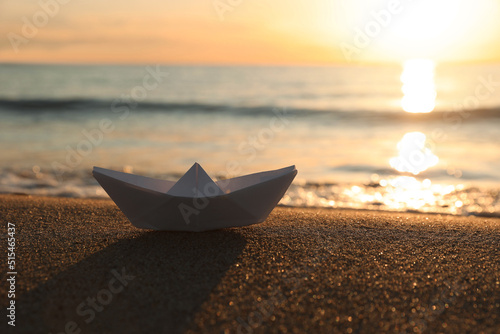White paper boat on sand near sea at sunset, space for text
