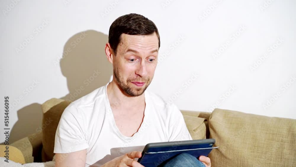 Young man working at living room. Home vacation sofa portrait. Blogger video. Alone in interior. Happy emotion. Smiling male person. Lifestyle action. House light background Young man working at living room. Home vacation sofa portrait. Blogger video. Alone in interior. Happy emotion. Smiling male person. Lifestyle action. House light background