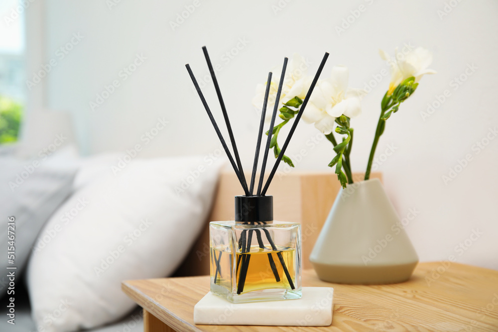 Reed diffuser and vase with bouquet on wooden nightstand in bedroom - obrazy, fototapety, plakaty 