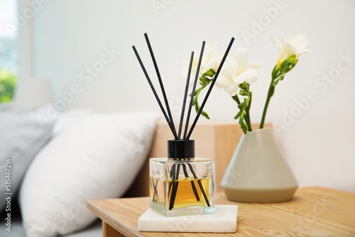 Reed diffuser and vase with bouquet on wooden nightstand in bedroom photo