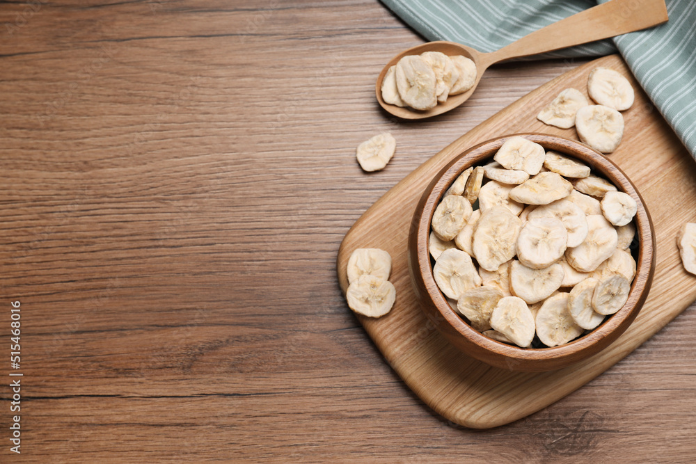 Bowl and spoon with dried banana slices on wooden table, flat lay. Space for text Bowl and spoon with dried banana slices on wooden table, flat lay. Space for text