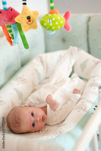 A newborn baby is lying in his crib and looking at toys suspended from above