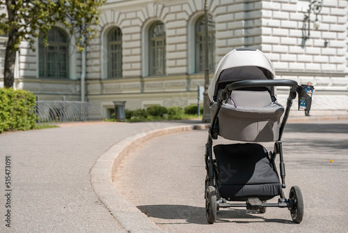 A gray stroller for a newborn baby stands in a summer green park