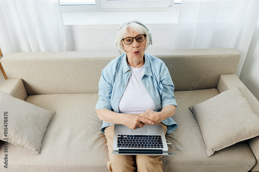 a pleasant, funny, adult woman talks emotionally via video link holding a laptop on her lap with headphones on her head while sitting in a comfortable environment at home