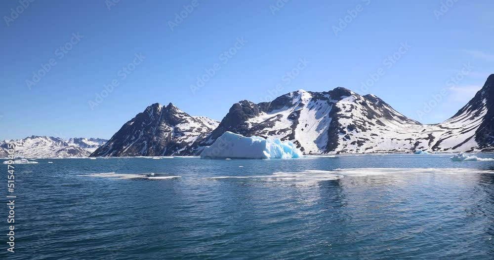 A rigid inflatable boat powers across the glacier lagoon at Kulusuk, Greenland - The result of global warming and climate change on our planet - Snowy mountain range reflection on the sea, Greenland A rigid inflatable boat powers across the glacier lagoon at Kulusuk, Greenland - The result of global warming and climate change on our planet - Snowy mountain range reflection on the sea, Greenland
