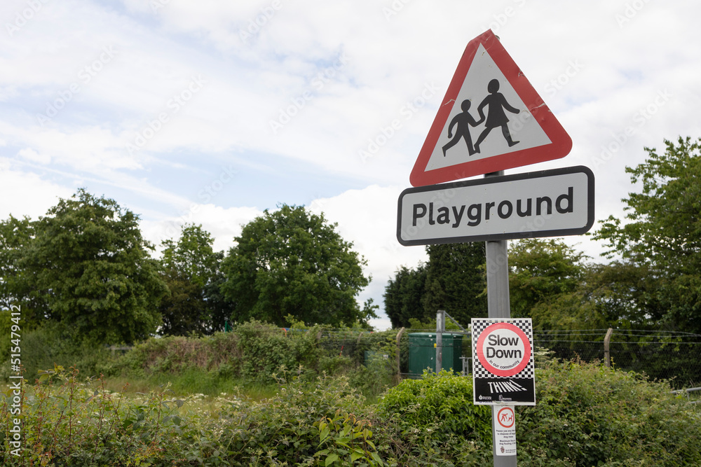  A British road sign signifying children going to or from school or a playground ahead. The sign is fixed to a lamppost with another sign saying ‘Reduce your speed’.