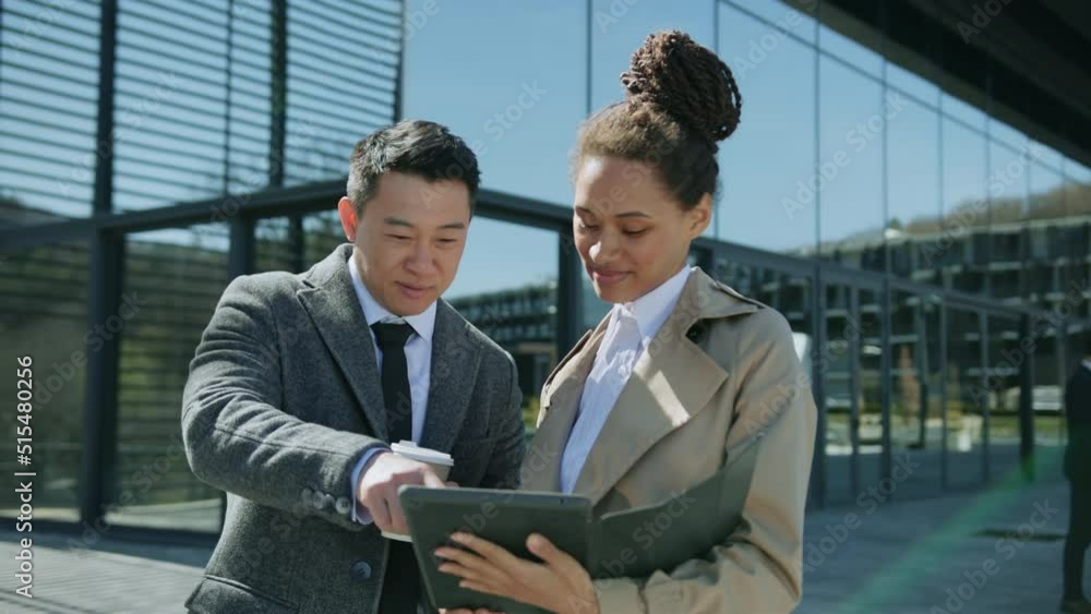 Smiling young business people stand talking spend time together outside. Woman holding tablet computer show to man. Sunlight. Slow motion Smiling young business people stand talking spend time together outside. Woman holding tablet computer show to man. Sunlight. Slow motion