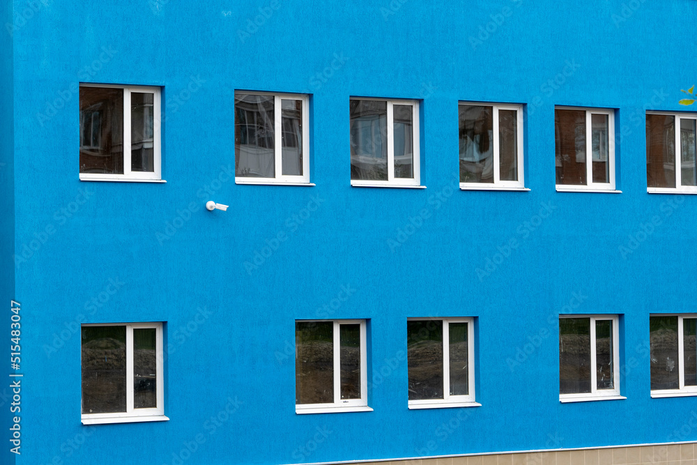 the wall of a new blue house with windows and a surveillance camera. 