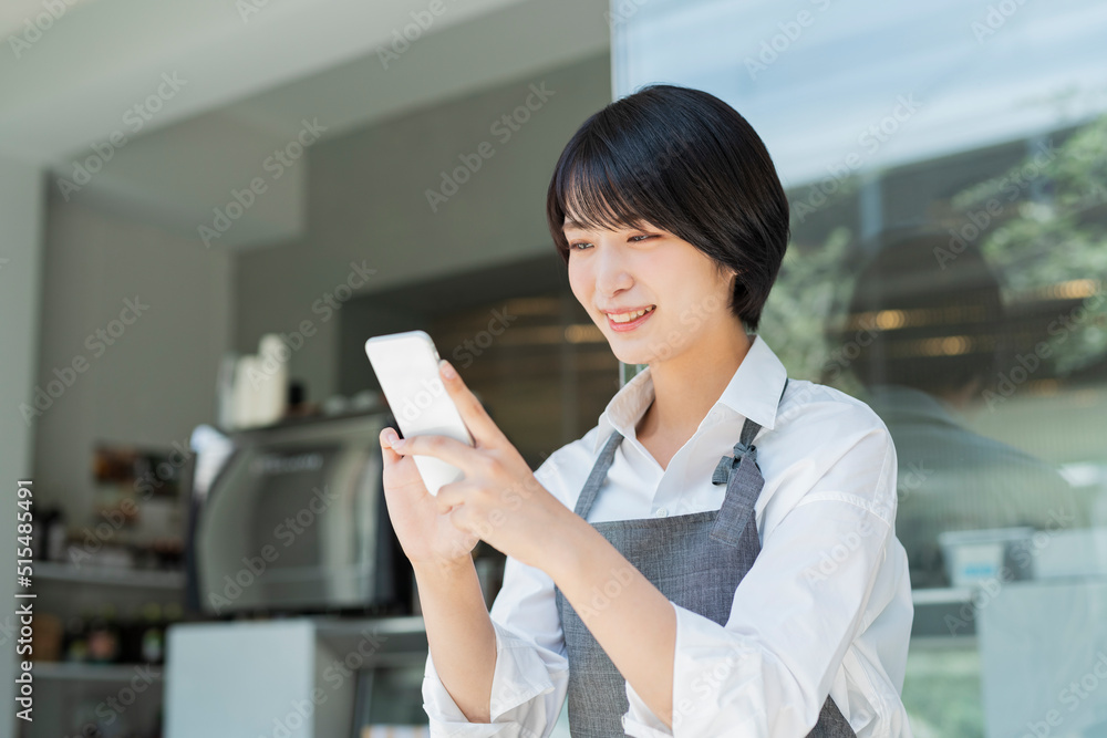 Obraz premium カフェ スマートフォンを使う女性スタッフ
