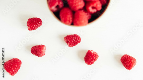 Fresh red raspberries in a paper cup on a white table background