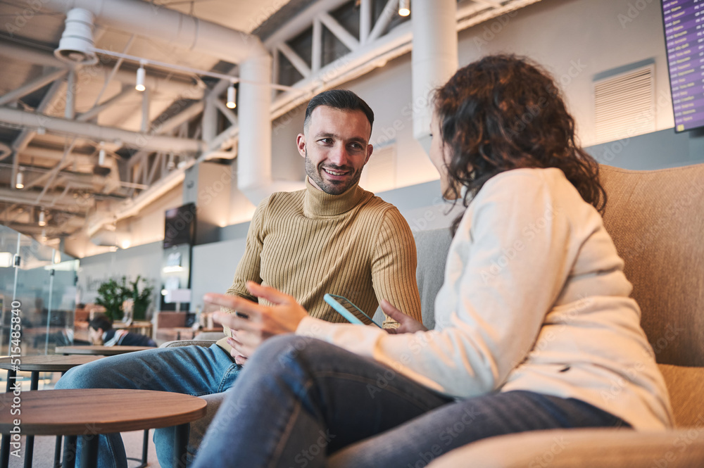 Happy young couple talking while sitting in VIP lounge of airport departure terminal waiting to board flight Happy young couple talking while sitting in VIP lounge of airport departure terminal waiting to board flight