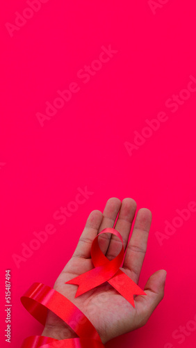 Hand holding a Red AIDS Ribbon with copy space for text isolated on red background