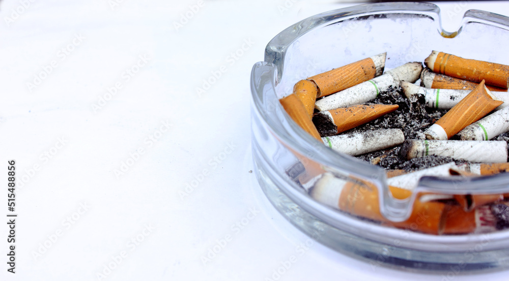 Lots of dirty used cigarette butts in an ashtray on a white background. Glass ashtray. Health, smoking, unhealth, Lung cancer. View from above. Copy text space Lots of dirty used cigarette butts in an ashtray on a white background. Glass ashtray. Health, smoking, unhealth, Lung cancer. View from above. Copy text space
