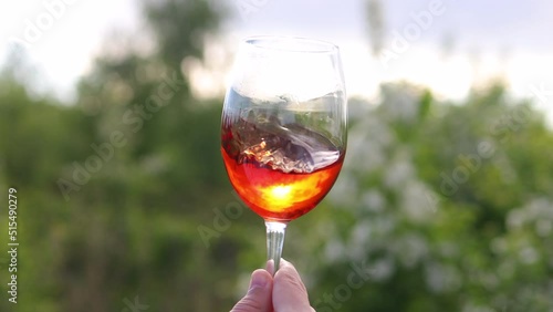 Glass with red drink in hand against the background of sunset.  
Sunny, summer evening, red wine. The concept of peace, love.